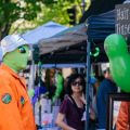 person in an alien costume looking at items in a vendor booth