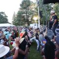 a performer sings into a mic in front of a dancing audience outdoors