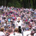 a man conducts a symphony outdoors with a large audience watching