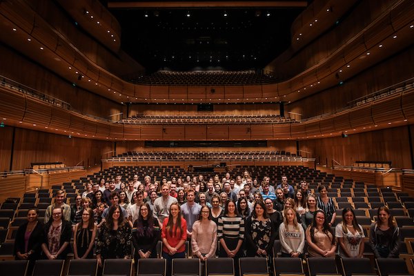 A large group of young singers standing in large auditorium