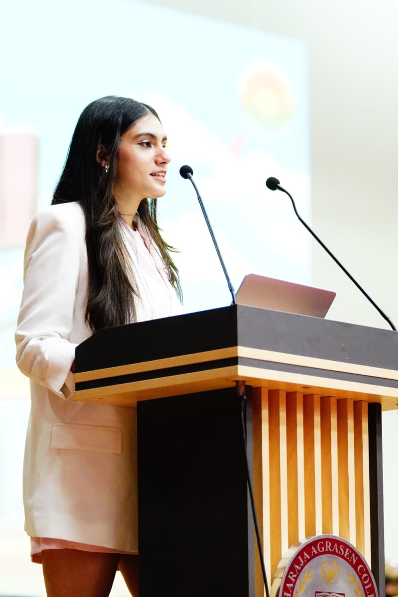 Lakshmi Cairae, Secretary General of Delhi MUN 1.0, speaks in a white blazer at the podium during the Delhi MUN 1.0 opening session
