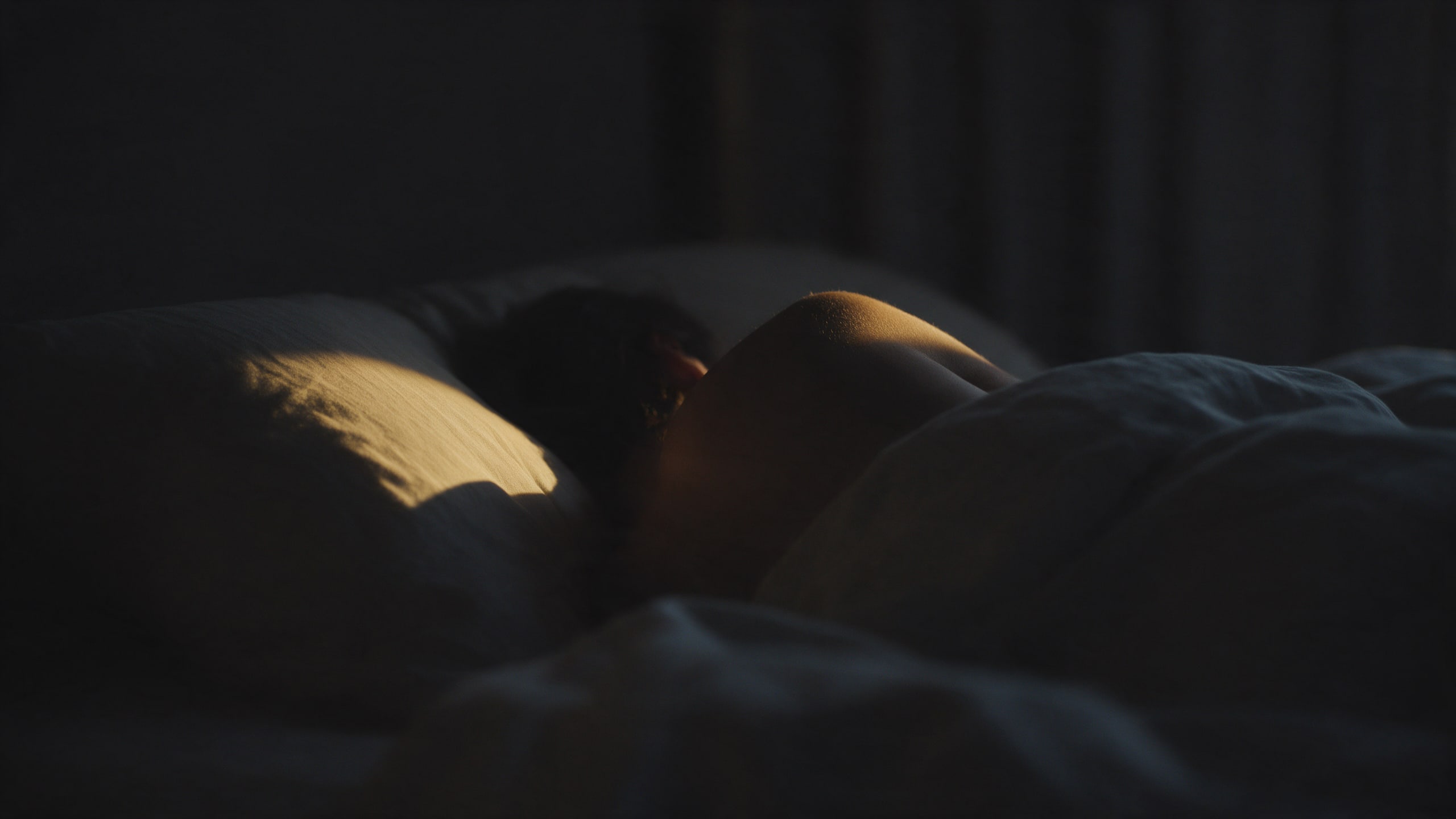 Persona durmiendo de costado en una habitación en penumbra, con una franja de luz cálida sobre la almohada — el descanso profundo que el bruxismo interrumpe