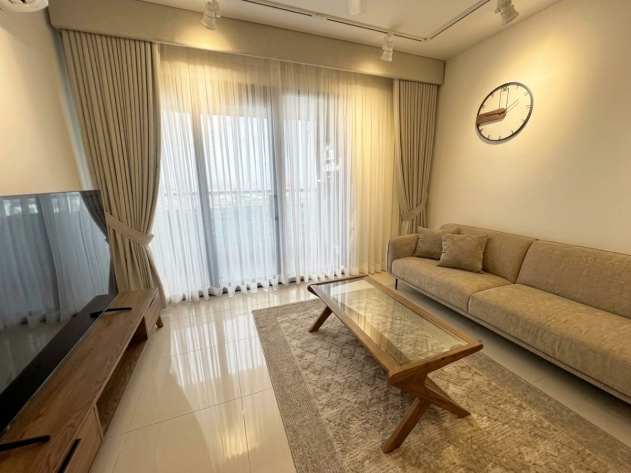 Bright furnished living room with sofa, TV, coffee table and floor-to-ceiling curtains at The Alcoves Cebu