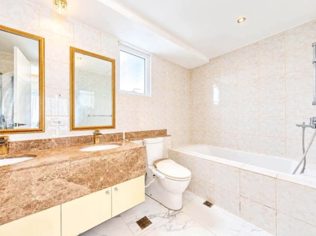 Bathroom with double vanity, gold-framed mirrors, marble countertop and bathtub in Marco Polo Residences condo, Cebu City