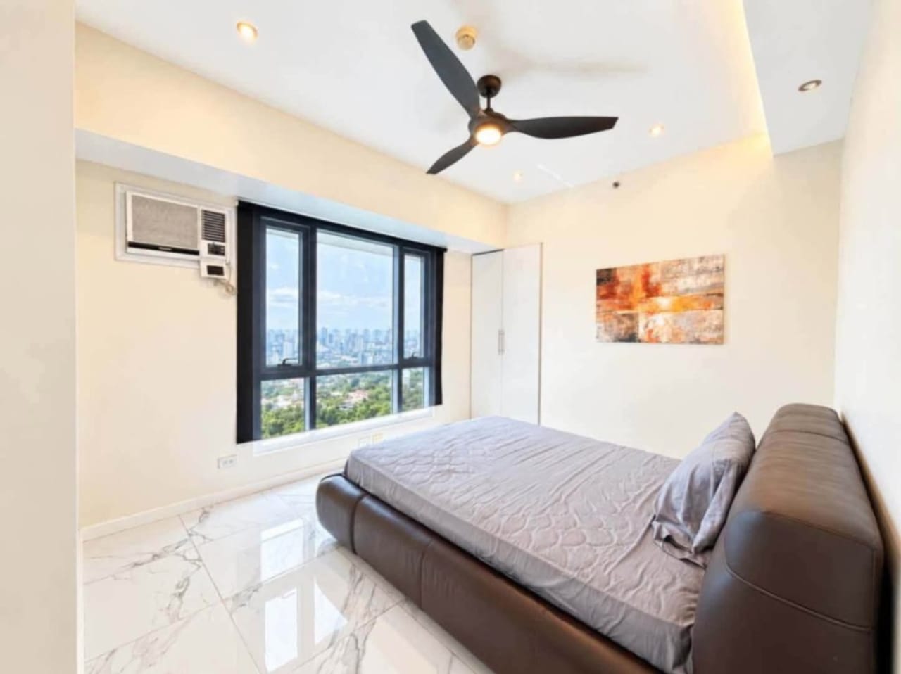Bedroom with ceiling fan, wardrobe and floor-to-ceiling window overlooking Cebu City skyline and greenery