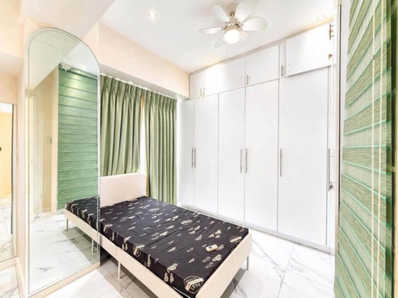 Furnished bedroom with built-in white wardrobe, green curtains and arched mirror at Marco Polo Residences