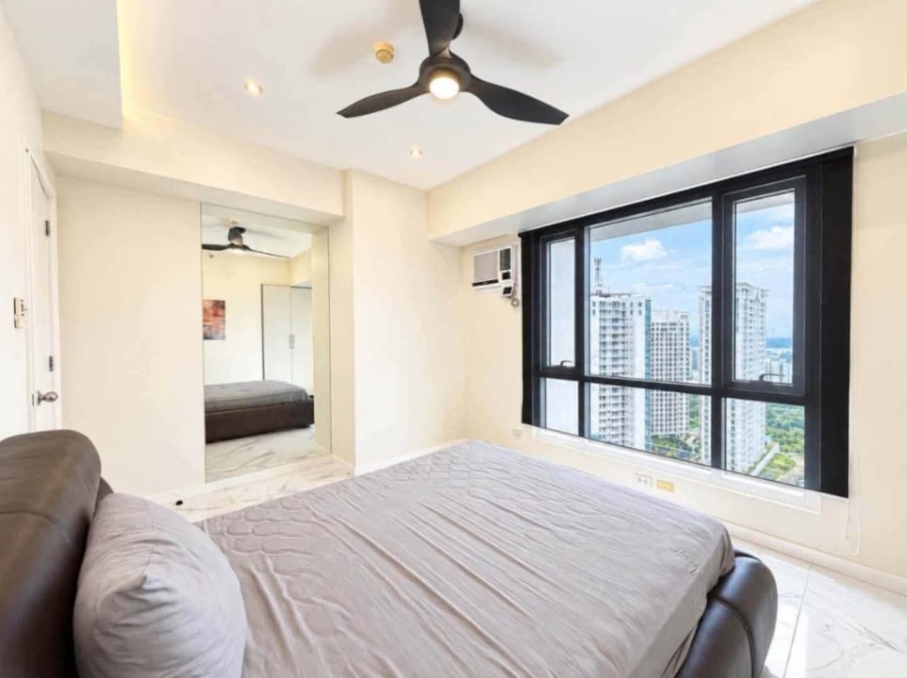 Bedroom with leather bed, ceiling fan and high-floor window view of Cebu City towers at Marco Polo Residences