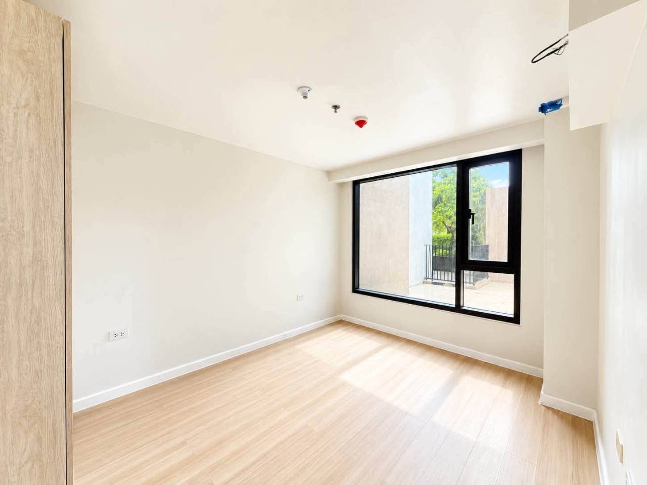 Bright condo bedroom with large glass window and wood flooring in Mandani Bay, Mandaue City
