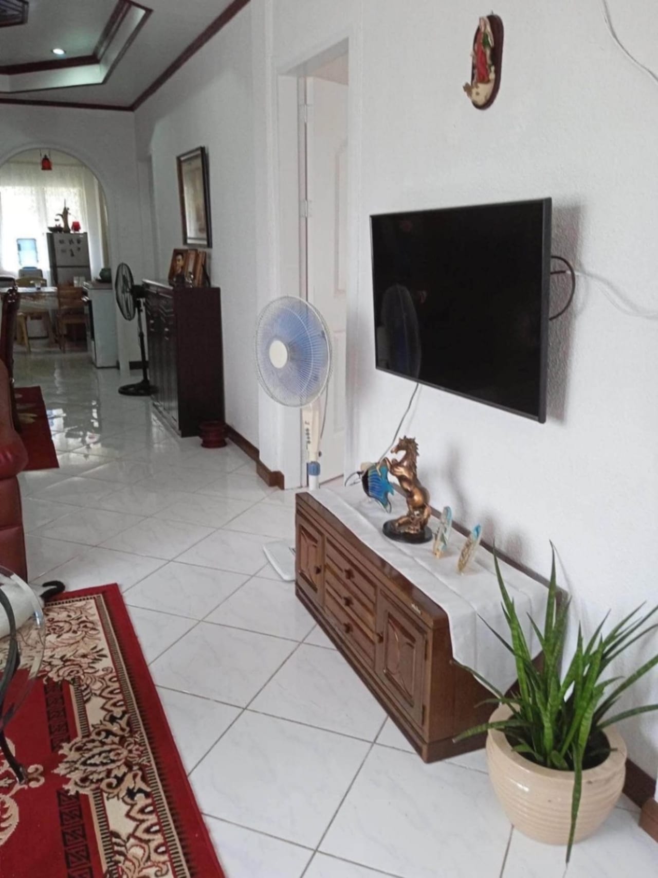 Living room with wall-mounted television and wooden cabinet in a furnished house for sale in Cordova, Cebu.