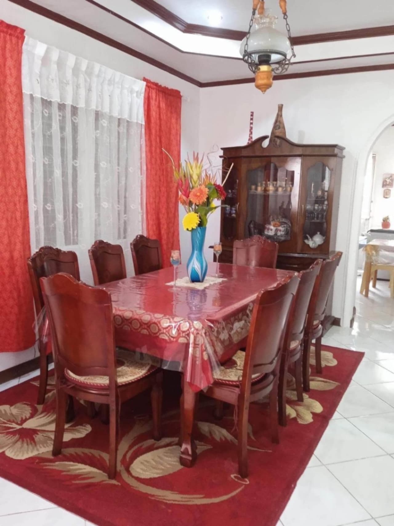Dining room with wooden dining table, chairs, and red curtains in a furnished house for sale in Buagson, Catarman, Cordova, Cebu.