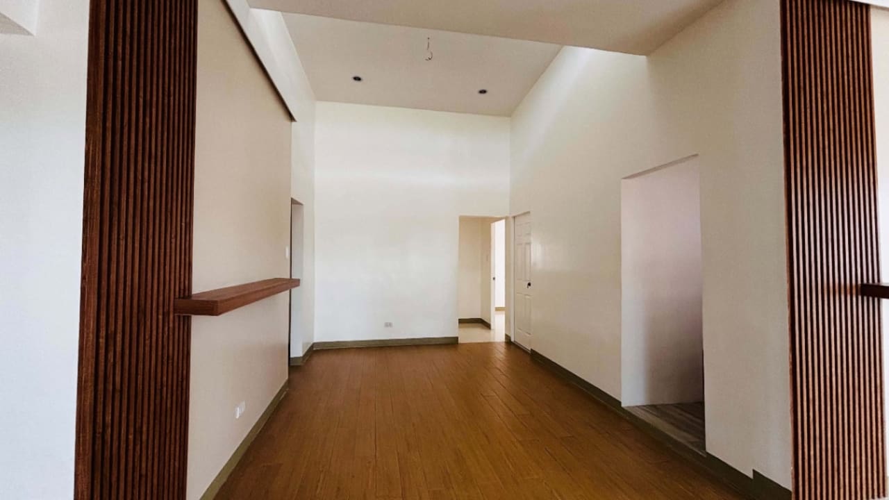 Empty interior hallway with white walls, brown wooden flooring, and doorways in a modern tropical bungalow for sale in Yati, Liloan, Cebu.