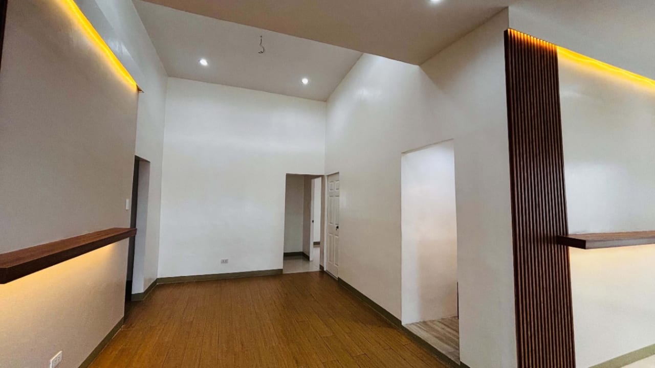 Spacious empty living area with wooden flooring, recessed ceiling lights, and white walls in a newly renovated bungalow for sale in Liloan, Cebu.