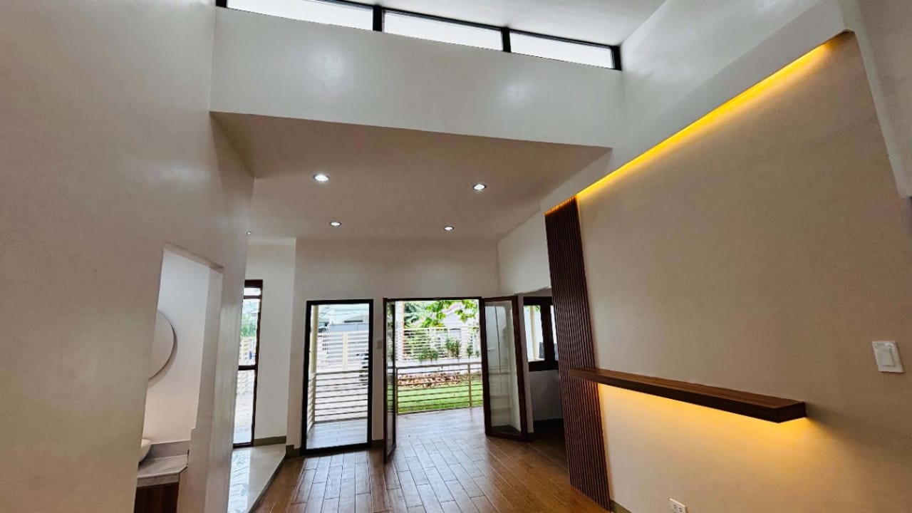 Modern living room with recessed ceiling lights, decorative illuminated wall panel, and sliding glass doors overlooking the outdoor area in Yati, Liloan.
