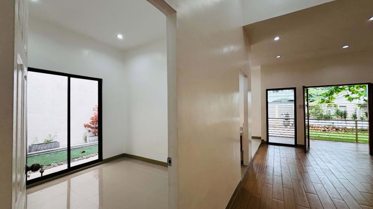 Empty bedroom with white walls, wooden flooring, and a large sliding glass window overlooking the lawn in a bungalow for sale in Liloan, Cebu.