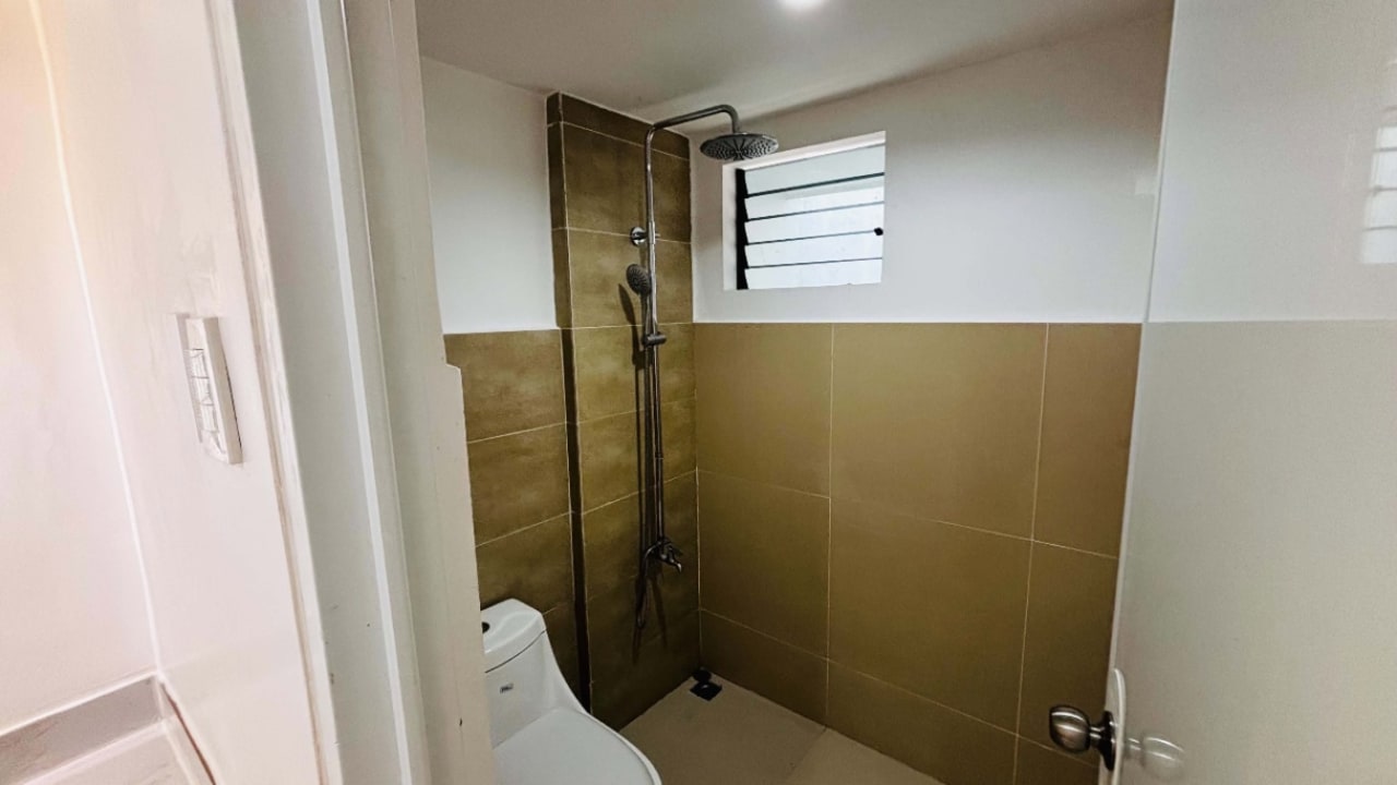 Bathroom with glass-enclosed shower area and neutral wall tiles in a modern tropical bungalow for sale in Yati, Liloan, Cebu.