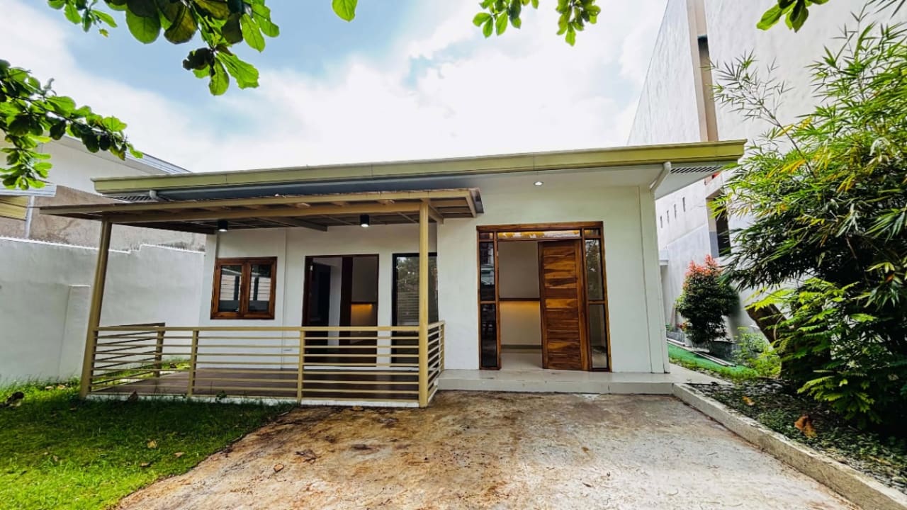 Front exterior of a modern tropical bungalow with a covered porch, driveway, landscaped greenery, and contemporary facade in St. Joseph Heights Subdivision, Yati, Liloan, Cebu.