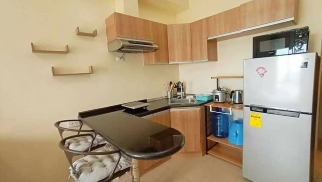Kitchen area with built-in wooden cabinets, black countertop, refrigerator, and dining table in a 26 sqm studio condominium at Avida Riala Tower 3, Cebu IT Park.