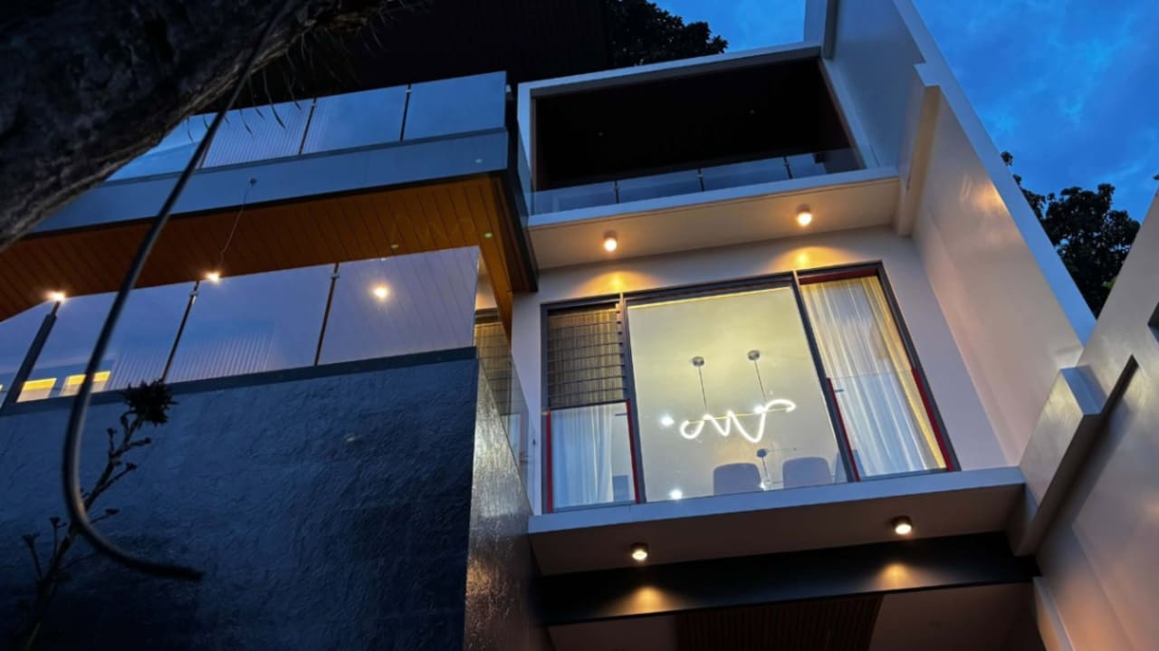 Modern three-storey house exterior at dusk featuring large glass windows, contemporary architecture, and illuminated interiors in Cebu City.