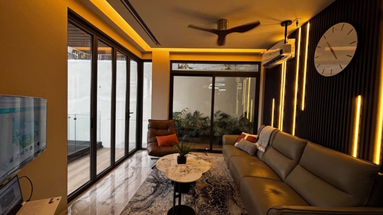 Open-plan living and dining area with a wooden dining table, upholstered chairs, warm accent lighting, and large glass doors in a modern Cebu City home.