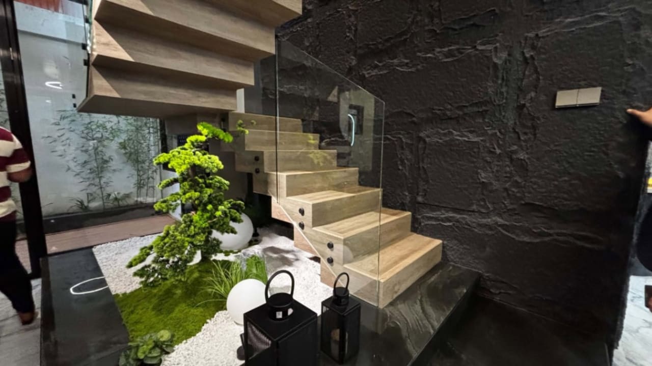 Modern staircase with floating wooden steps, dark stone accent wall, recessed lighting, and indoor plants in a contemporary three-storey Cebu City home.