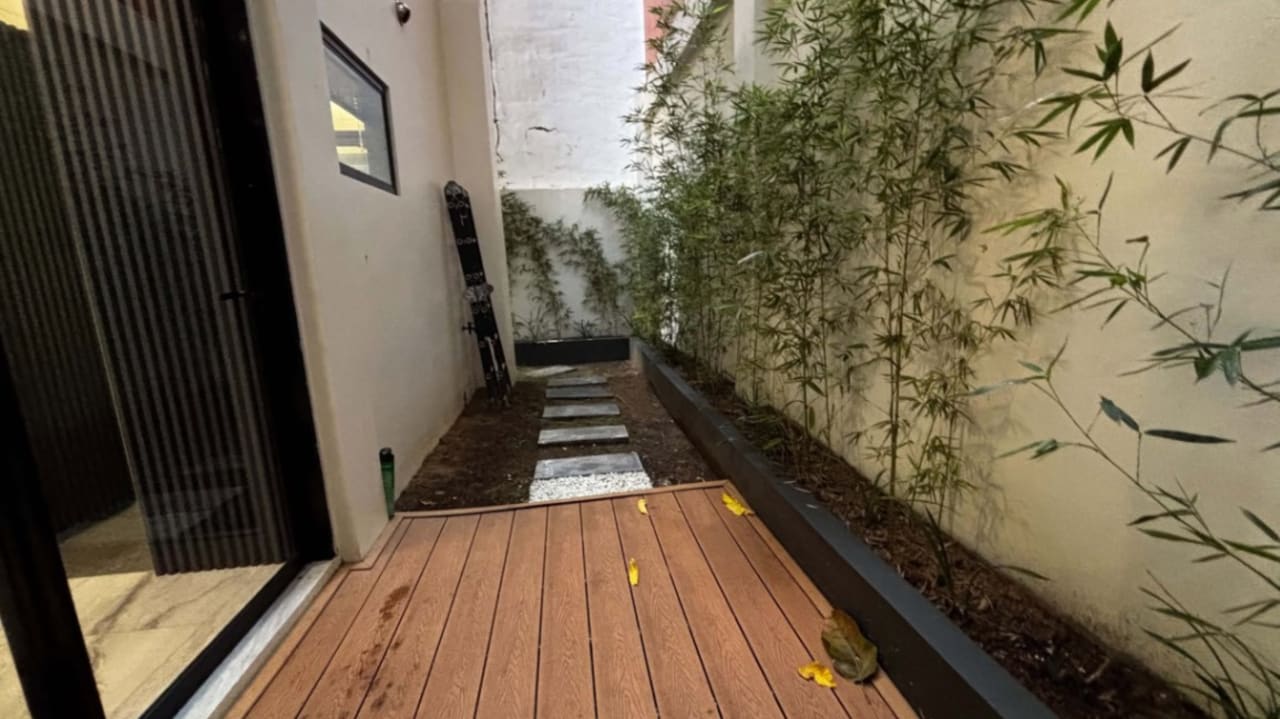 Narrow outdoor side passage with wood-look flooring, decorative greenery, textured walls, and a glass door in a modern house in Cebu City.