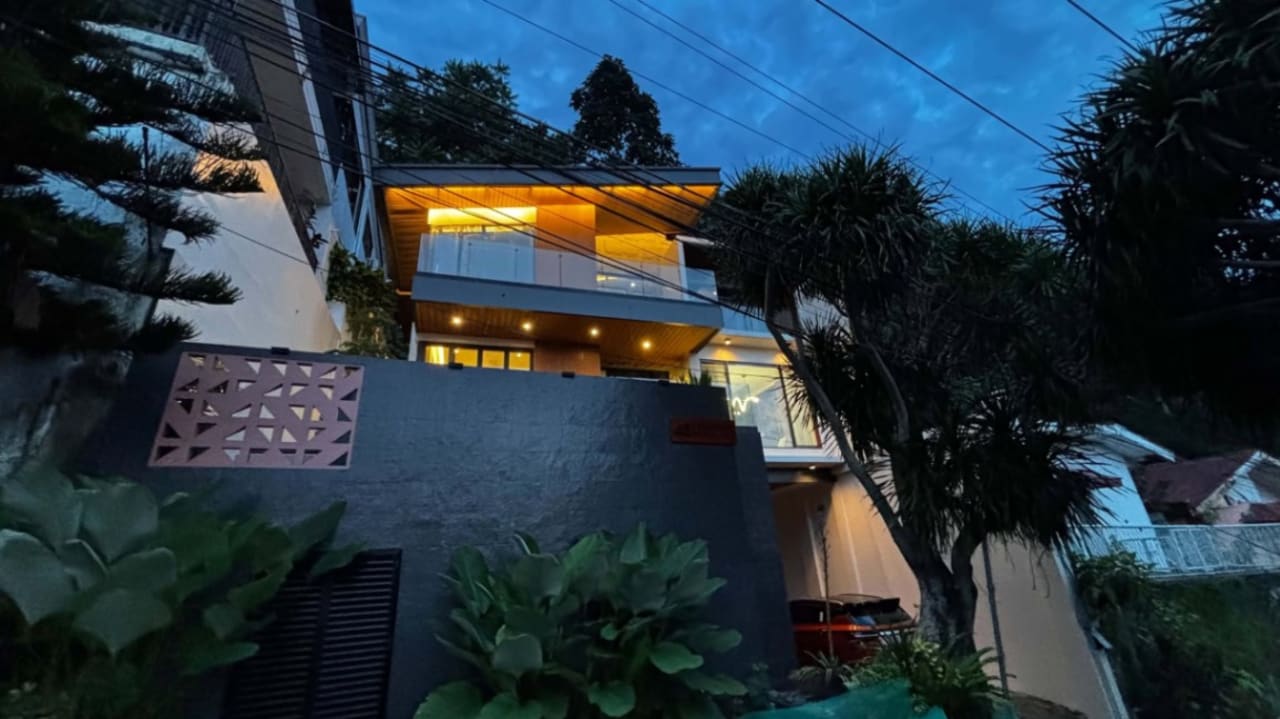 Contemporary three-storey house viewed from outside at dusk, featuring illuminated windows, modern architectural lines, and a concrete perimeter wall in Cebu City.