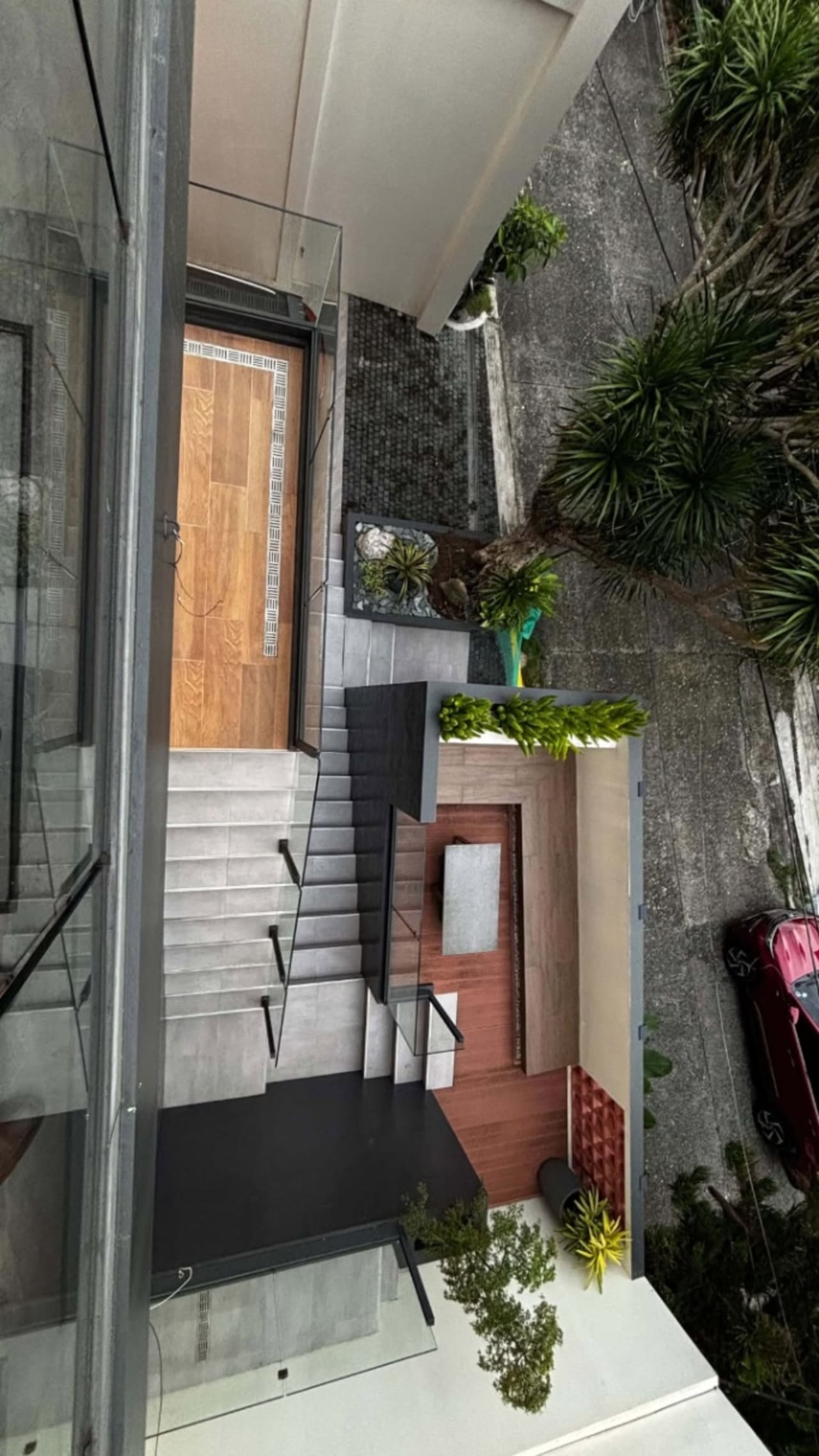 Exterior entrance with concrete steps, wooden front door, glass panels, potted plants, and textured stone walls at a modern house for sale in Cebu City.