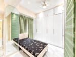 Furnished bedroom with built-in white wardrobe, green curtains and arched mirror at Marco Polo Residences