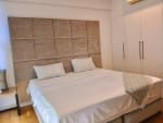Bedroom with a white bed, padded beige headboard, built-in wardrobe, and air conditioning in a 1-bedroom condo for sale in Cebu Business Park.