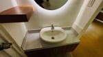 Modern bathroom vanity with round mirror, white countertop basin, and wooden shelving in a bungalow at St. Joseph Heights Subdivision, Yati.