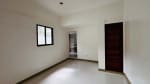 Empty bedroom with white walls, a black-framed window, tiled flooring, and a wooden door in a renovated house for sale in Yati, Liloan.