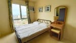 Bed beside a large window with curtains and wooden dressing table in a fully furnished studio condo for sale in Cebu IT Park.