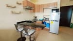 Compact kitchen with wooden overhead cabinets, black countertop, electric stove, refrigerator, and dining table in a fully furnished studio condo for sale at Avida Riala Tower 3.