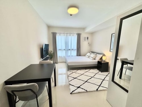 Fully furnished studio interior with bed, dining table, TV and large window at JTower Residences Mandaue