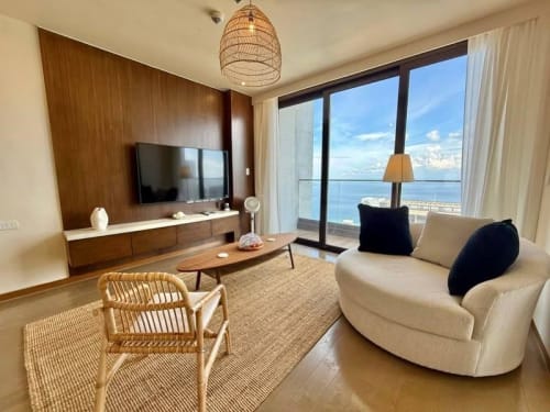 Living room with curved sofa, wooden coffee table, television, and floor-to-ceiling windows in a fully furnished condo for sale in Punta Engaño, Cebu.