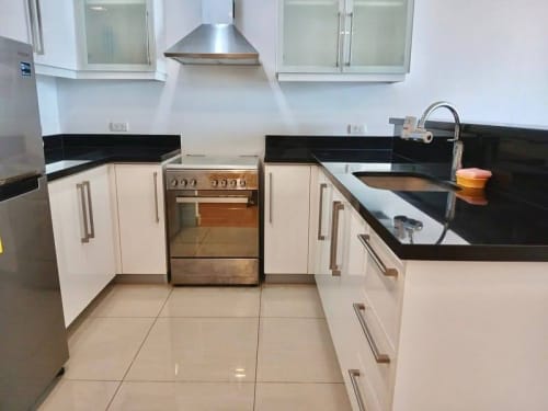 Modern U-shaped kitchen with white cabinets, black countertops, stainless steel range hood, and built-in stove in a Cebu City condominium.