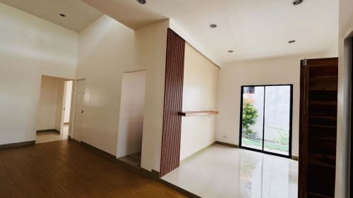 Open-plan bungalow interior with polished wooden flooring, white walls, and large sliding glass doors leading to the outdoor area in St. Joseph Heights, Liloan.