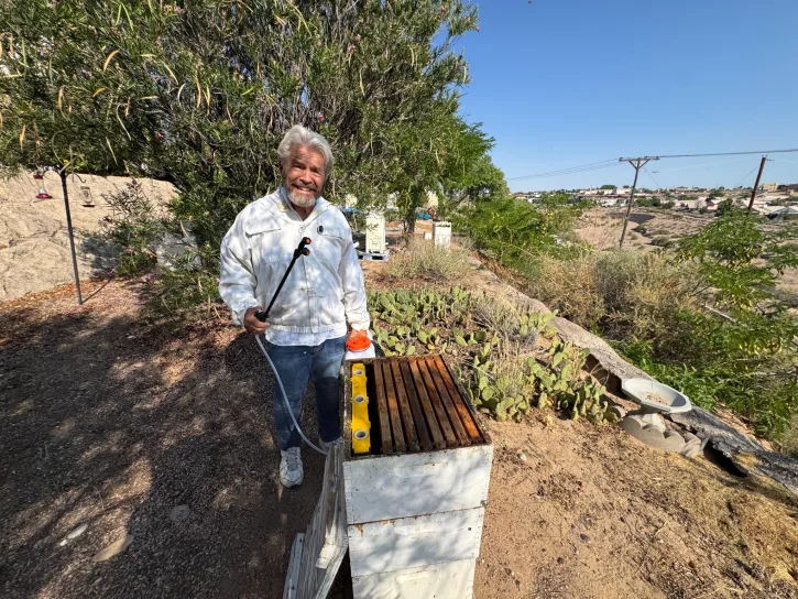 Hobbyist beekeeper Steve Stucker using an ApiVera backpack mister beside his hives