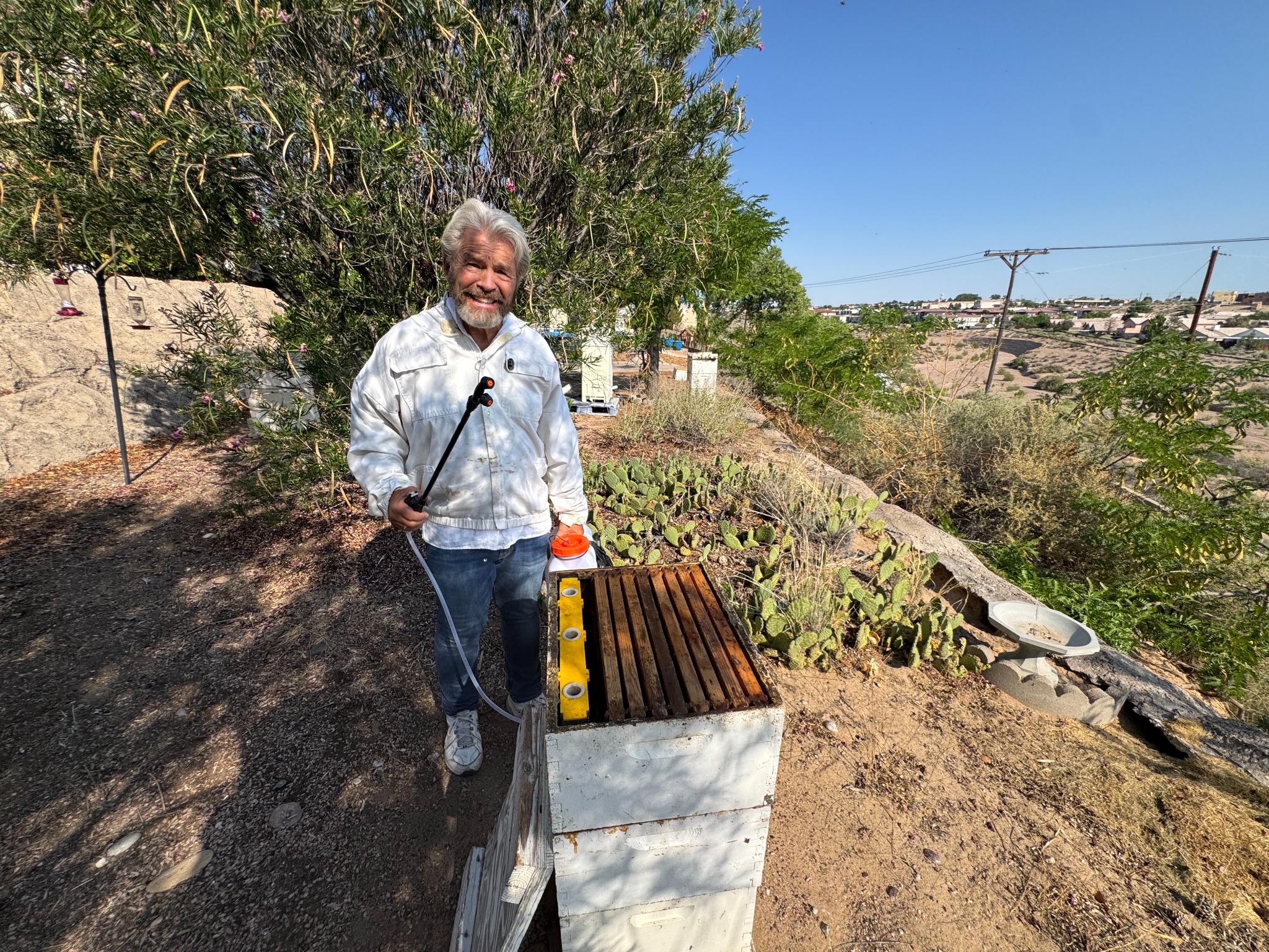 Hobbyist beekeeper Steve Stucker using an ApiVera backpack mister beside his hives