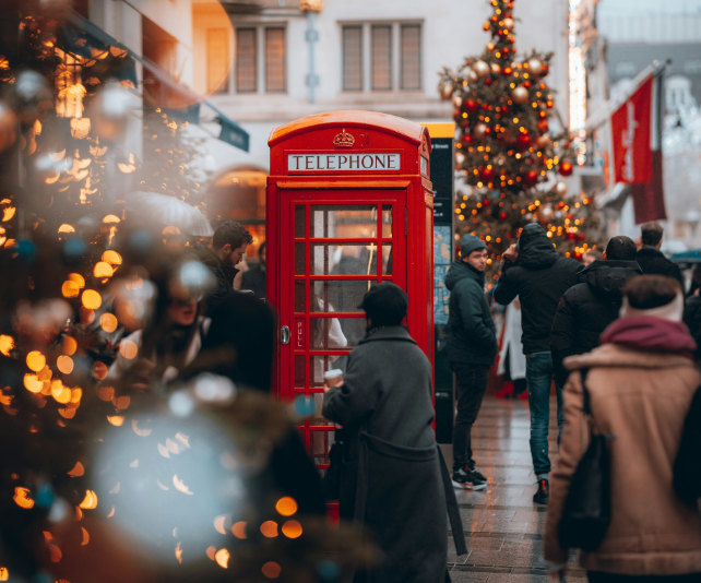 A red postbox surrounded by Christmas trees and people in coats.