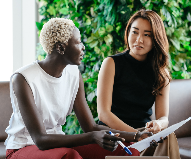 Two women discussing work in an office with a green background