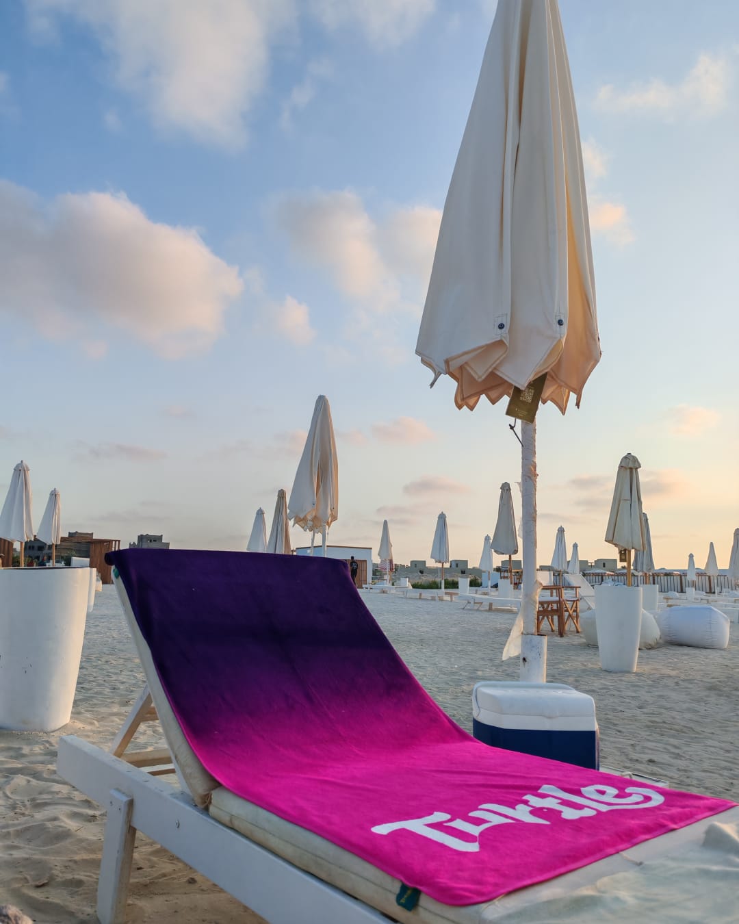 A Turtle SUNDAZE beach towel in Magenta Drift, laid over a sunbed in the late afternoon
