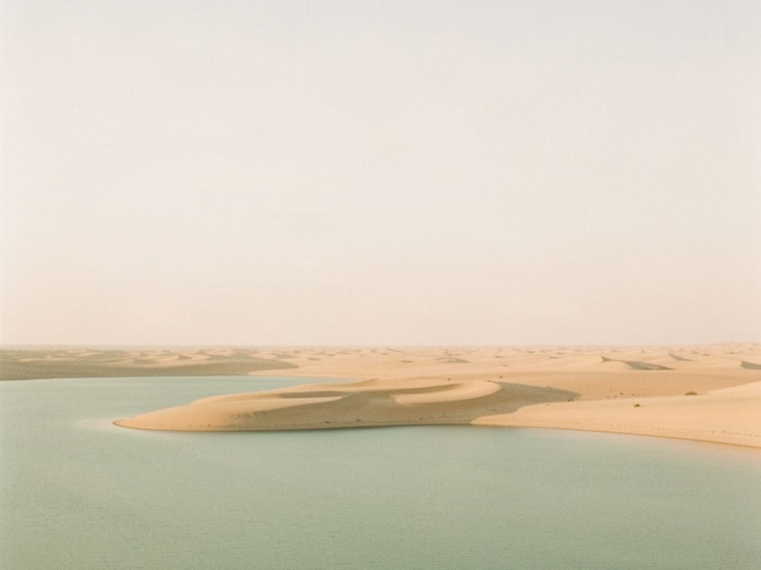 Pale dunes meeting still green water under a wide hazy sky