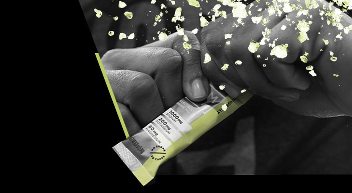 Hands tearing open an electrolyte packet with scattered salt particles, in black and white with lime accents
