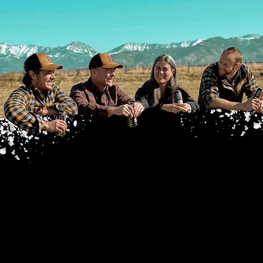 Four LMNT founders lean on a fence against snow-capped mountains and prairie grass under a turquoise sky