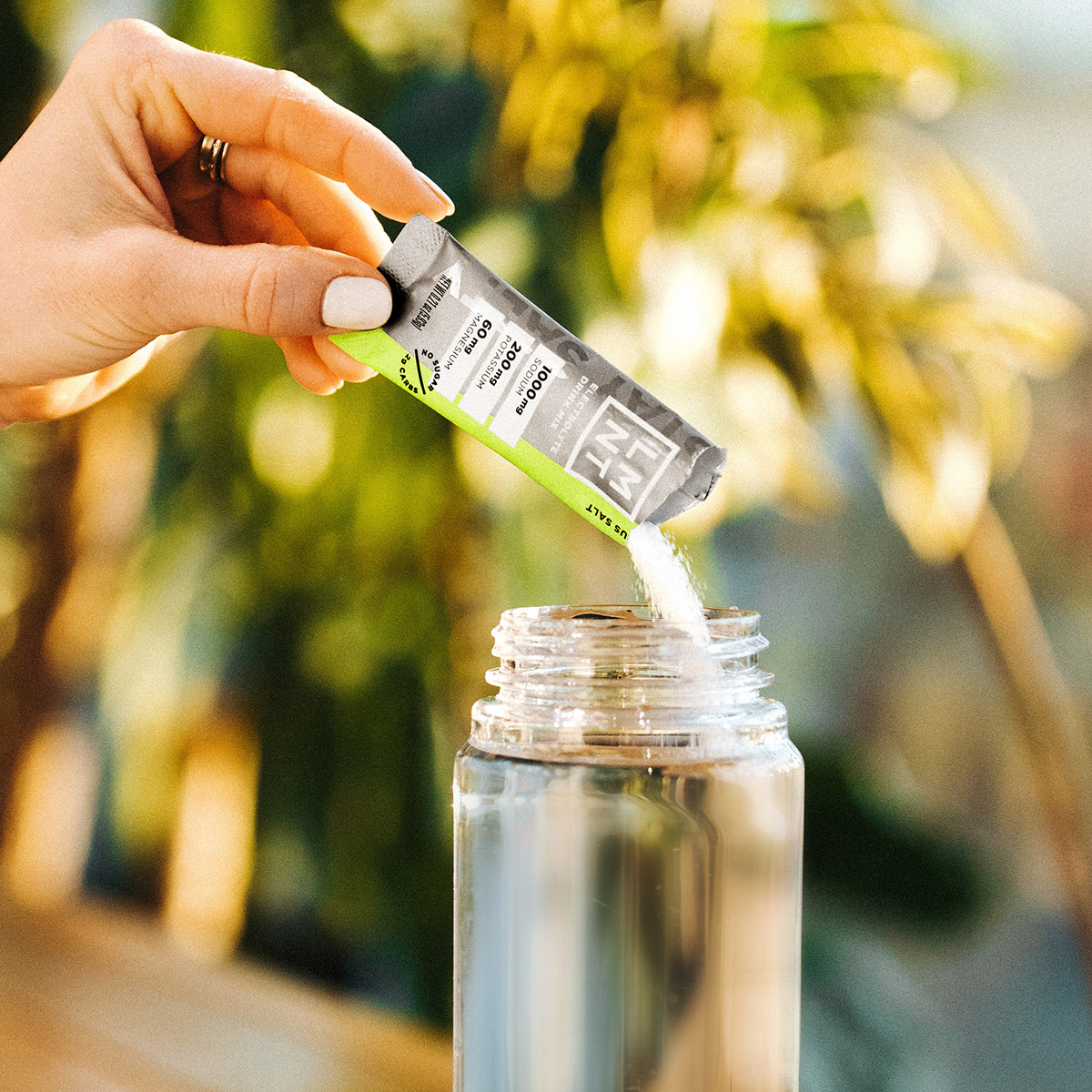 Mind Pump's Adam Schafer adding a Watermelon electrolyte packet to his clear water bottle while resting his left arm on a table.