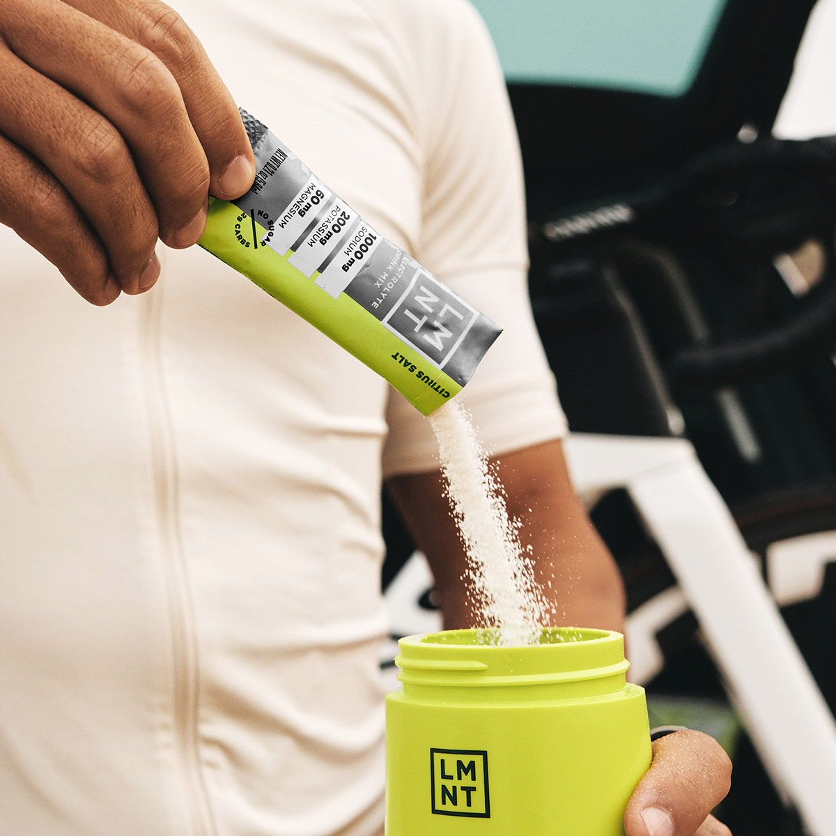 Mind Pump's Adam Schafer adding a Watermelon electrolyte packet to his clear water bottle while resting his left arm on a table.