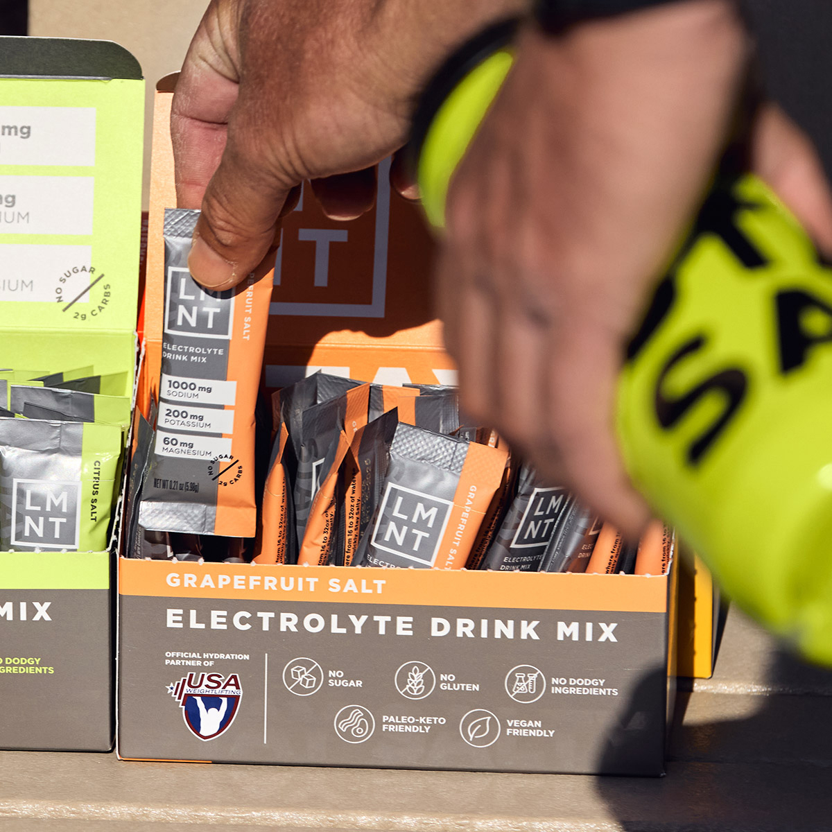 Hand selecting a LMNT electrolyte packet from a retail box containing only Grapefruit packets