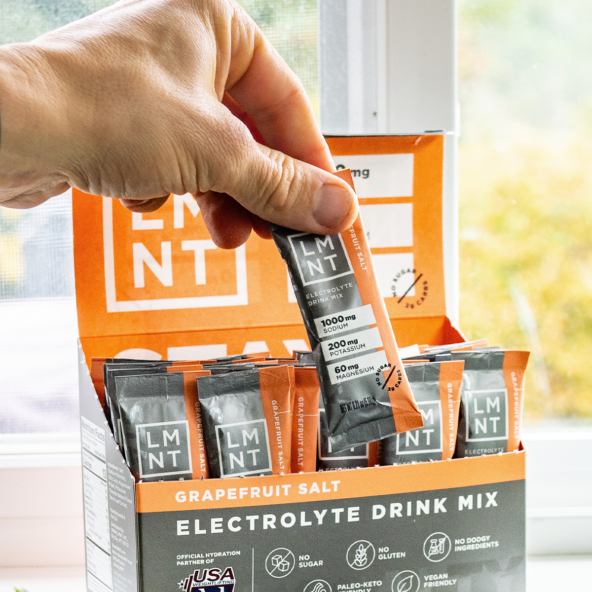 Hand selecting a LMNT electrolyte packet from a retail box containing only Grapefruit packets