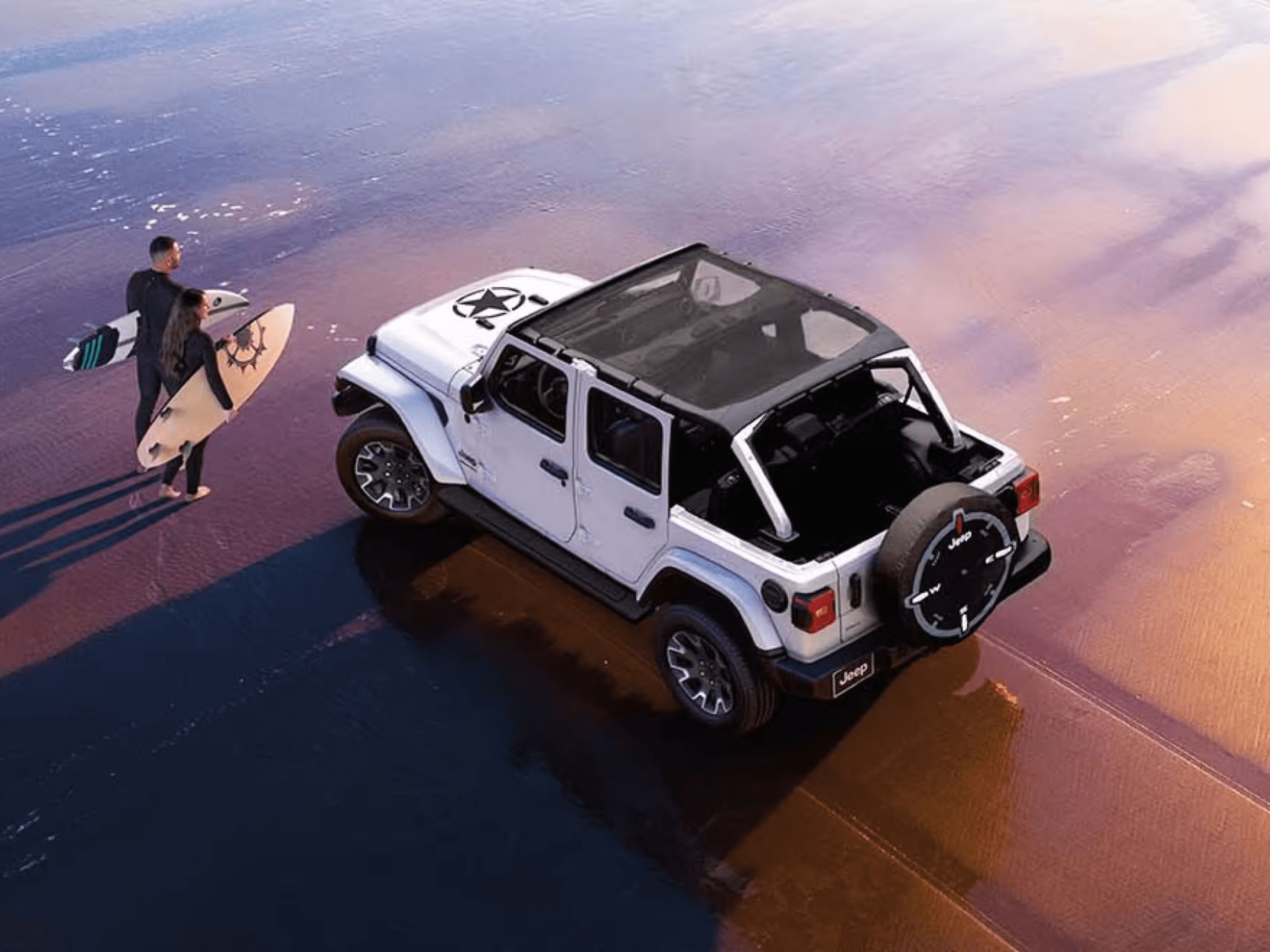 A white SUV sits on a reflective wet shore with two surfers standing nearby under a soft, colorful sky.